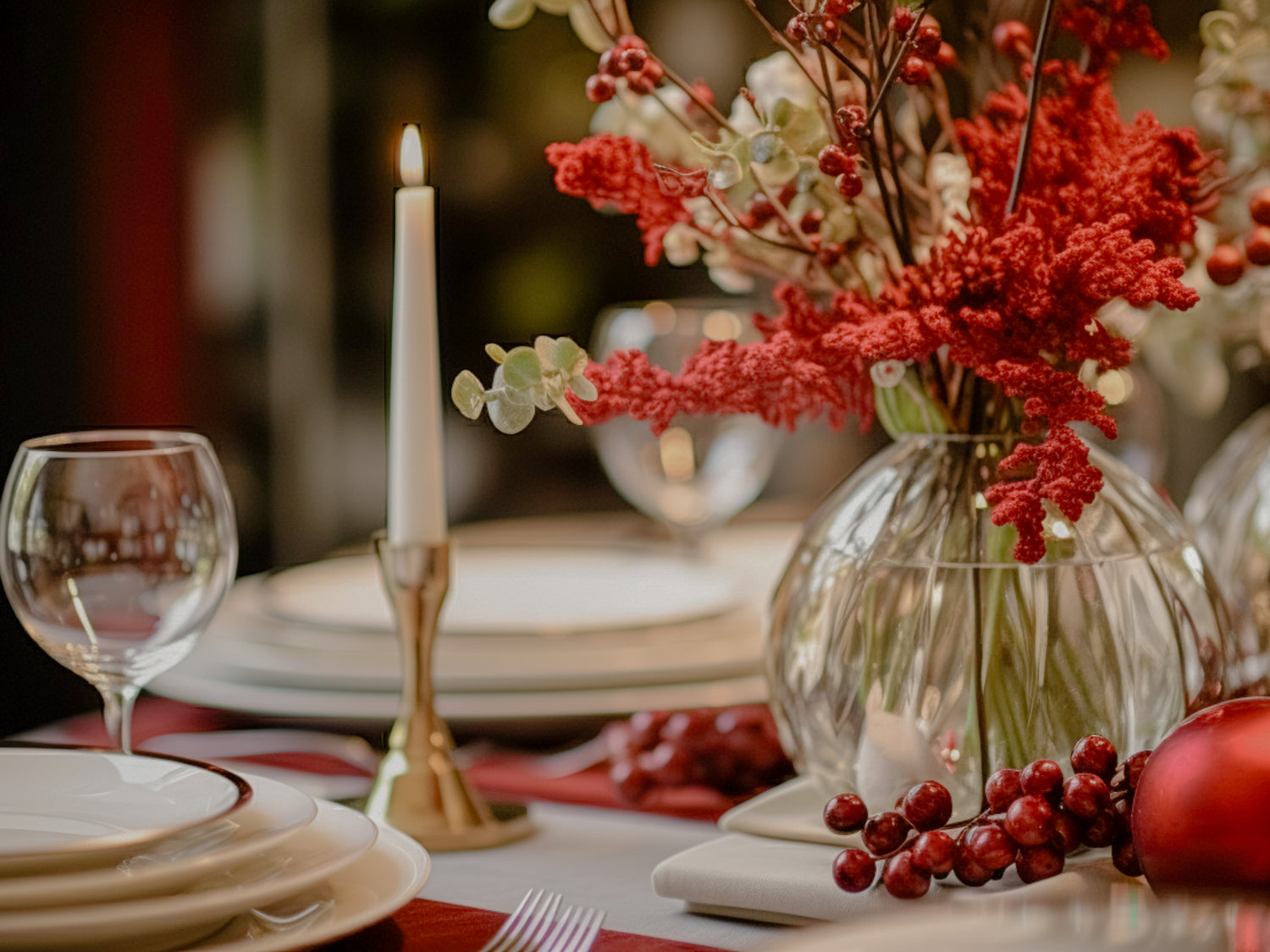 Decorative table setting with red flowers in a vase, candles, and plates.